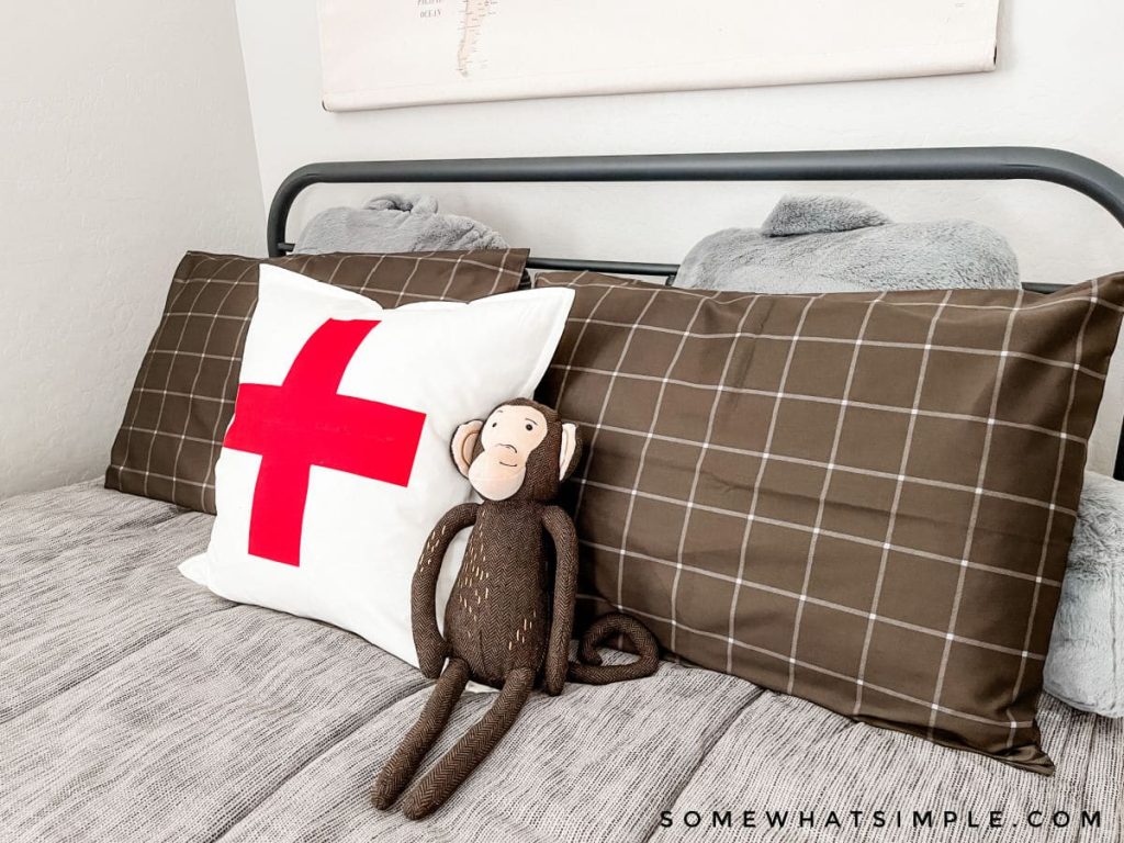 close up of a stuffed monkey on a bed with gray bedding and a swiss cross pillow