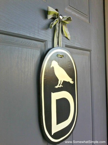 a crow monogram with the letter D on a piece of wood hanging from a door