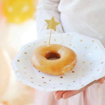 child holding a white plate with a glaze donut on it and a paper star on a stick stuck to the side