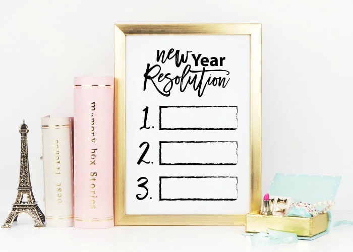 framed print with new years resolutions next to a stack of books and some office supplies
