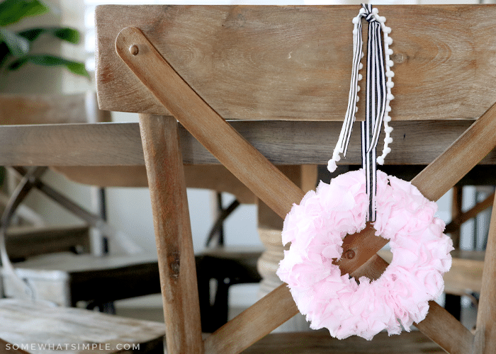 pink ruffle ribbon wreath hanging on the back of a brown chair