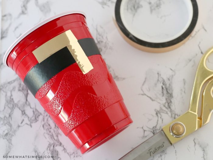 adding gold tape to a red cup to look like Santa's buckle