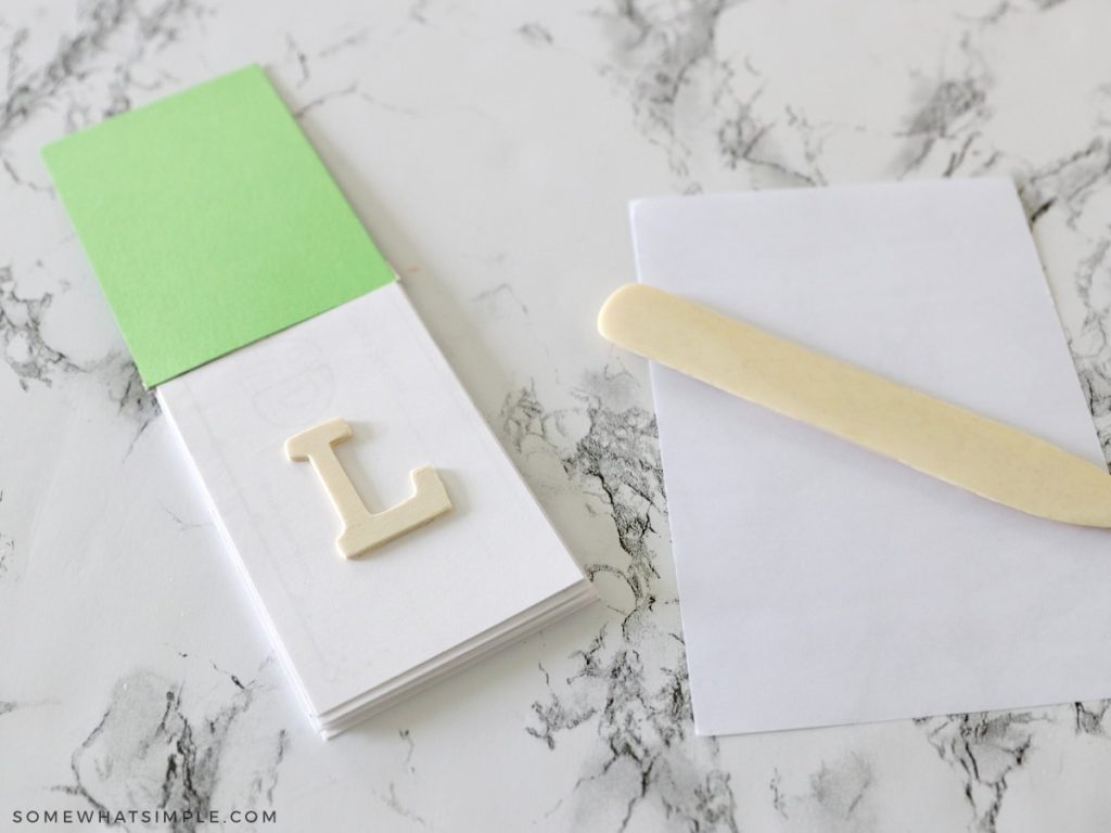 green notepad with a wood letter L getting ready to be embossed