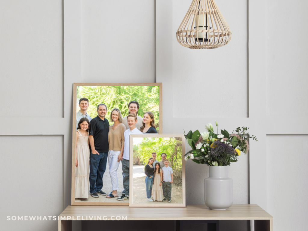 close up of a console table with framed family pictures and a plant and hanging lamp