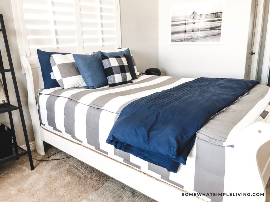 close up of a bed with gray and white striped bedding and a navy throw blanket