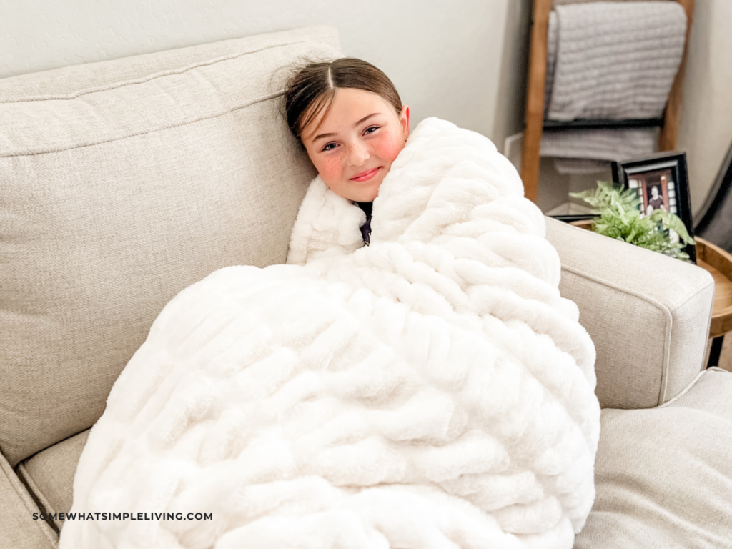 little girl sitting on a couch wrapped in a cozy blanket