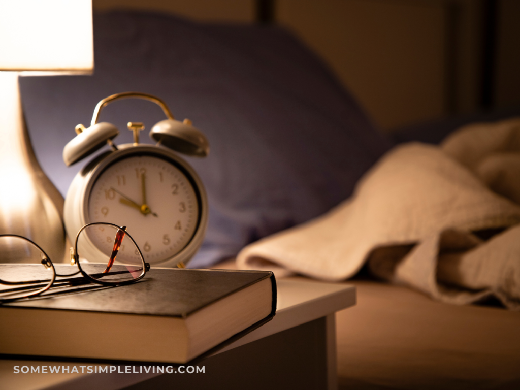 alarm clock next to reading glasses, a lamp, and a book