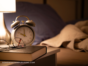 alarm clock next to reading glasses, a lamp, and a book